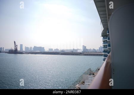 Ein riesiges Gebäude, viele Turmbaustellen mit Kränen und Gebäuden und dem Meer. Ansicht von der Bootstour mit gezeigtem Fenster. Abo Dhabi, Stockfoto