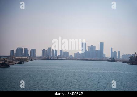 Ein riesiges Gebäude, viele Turmbaustellen mit Kränen und Gebäuden vor dem Meer. Blick von der Bootstour. Abo Dhabi, Vereinigte Arabische Emirate Stockfoto