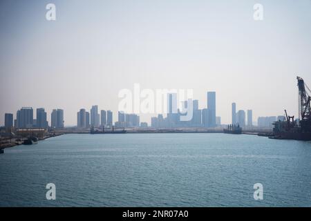 Ein riesiges Gebäude, viele Turmbaustellen mit Kränen und Gebäuden neben dem Parkplatz und dem Meer. Blick von der Bootstour. Abo Dhabi, Vereinigt Euch Stockfoto