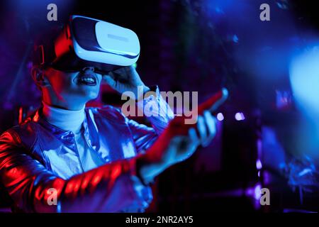Neon-Metaverse-futuristisches Konzept. Lächelnde, moderne Frau in der virtuellen Realität Brille interagiert mit der virtuellen Realität. Stockfoto