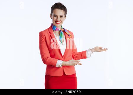 Fröhliche, elegante Stewardess vor weißem Hintergrund in Uniform, einladend. Stockfoto