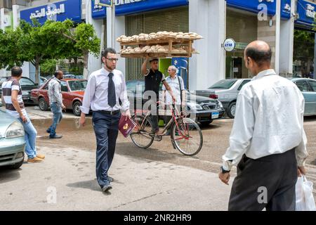 Ein Mann, der Aish Baladi, auch bekannt als ägyptisches Fladenbrot, mit seinem Fahrrad entlang einer belebten Straße in Kairo in Ägypten transportiert. Stockfoto