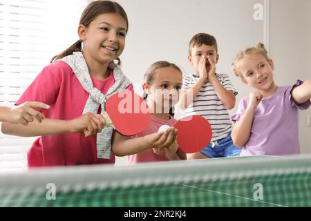 Süße glückliche Kinder, die drinnen Tischtennis spielen Stockfoto