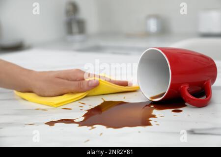 Eine Frau, die verschütteten Kaffee auf einem weißen Marmortisch in der Küche aufräumte Stockfoto