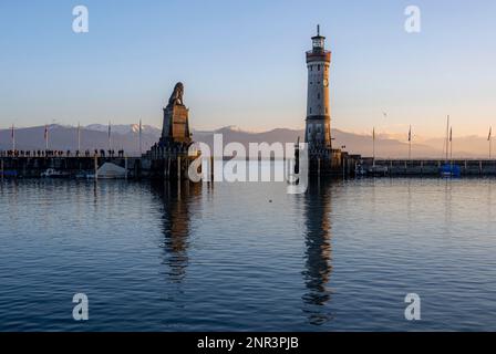 Hafeneingang zum Hafen von Lindau, Pier mit dem Leuchtturm von New Lindau und dem bayrischen Löwen, bei Sonnenuntergang, schneebedeckte Berge im Hintergrund, Lindau Island, La Stockfoto