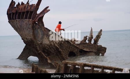 Ein Angler, der am Nachmittag auf Einem versunkenen Schiffswrack am Strand in Muntok Town steht Stockfoto