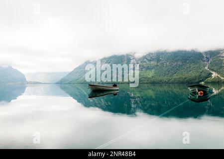 Einsame Boote beruhigen See mit nebligen Berg Hintergrund Stockfoto
