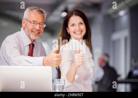 Lächelnde, erfolgreiche Geschäftsleute, die mit Daumen nach oben zeigen, unterschreiben das Büro Stockfoto