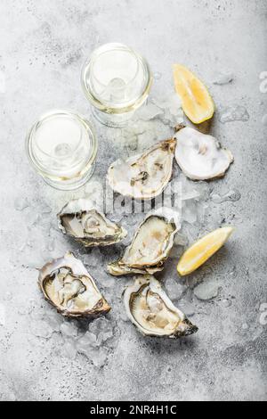 Nahaufnahme von einem halben Dutzend frischer Austern und Muscheln mit Zitronenkeilen, zwei Gläsern Weißwein oder Champagner, Blick von oben, grauer rustikaler Beton Stockfoto