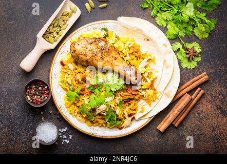 Ein Blick von oben auf Biryani Chicken mit Basmati-Reis, Gemüse, Koriander und Naan-Brot in der Schüssel, ein traditionelles indisches würziges Gericht, auf rustikalem Steinbackgro Stockfoto