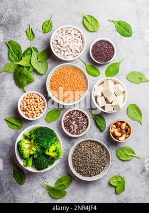 Draufsicht der verschiedenen veganen Proteinquellen: Bohnen, Linsen, Quinoa, Tofu, Gemüse, Spinat, Nüsse, Kichererbsen, Reis, Stein, rustikaler Hintergrund. Stockfoto