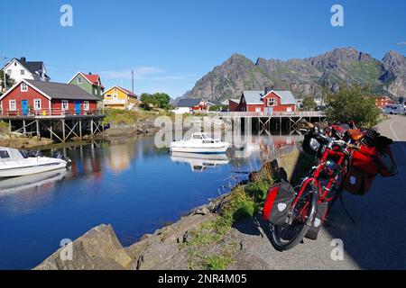 Bunte Häuser im kristallklaren Meerwasser, vollgepacktes Touring-Fahrrad, Fahrradtourismus, kleine Freizeitboote und Turner, Henningsvaer Stockfoto