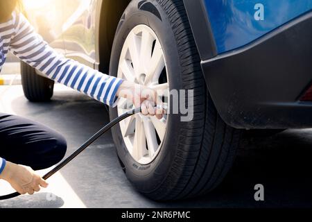 Frau bläst den Reifen auf. Frau, die den Reifendruck überprüft und Luft in den Reifen des Autorads pumpt. Autowartung zur Sicherheit vor der Reise. Stockfoto