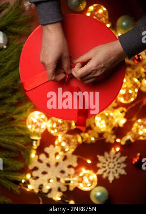 Umgeben von Weihnachtsspielzeug auf roter Geschenkbox, Band zum Binden der Hände Stockfoto