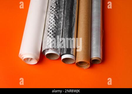 Rollen aus Aluminiumfolie, Backpapier und Lebensmittelfolie auf farbigem Hintergrund Stockfoto