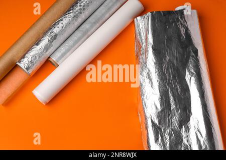 Rollen aus Aluminiumfolie, Backpapier und Lebensmittelfolie auf orangefarbenem Hintergrund Stockfoto