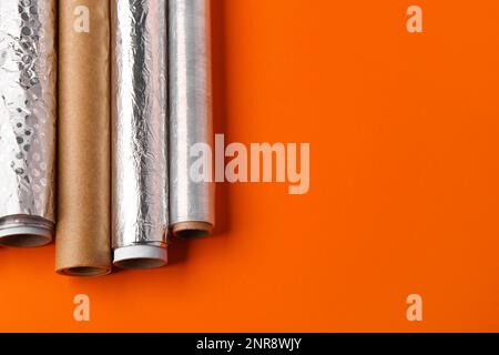 Rollen aus Aluminiumfolie, Backpapier und Lebensmittelfolie auf farbigem Hintergrund Stockfoto