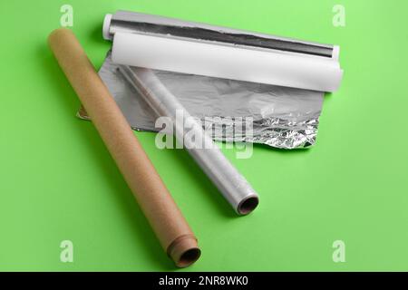 Rollen aus Aluminiumfolie, Backpapier und Lebensmittelfolie auf grünem Hintergrund Stockfoto