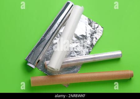 Rollen aus Aluminiumfolie, Backpapier und Lebensmittelfolie auf grünem Hintergrund Stockfoto