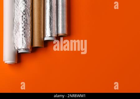 Rollen aus Aluminiumfolie, Backpapier und Lebensmittelfolie auf farbigem Hintergrund Stockfoto