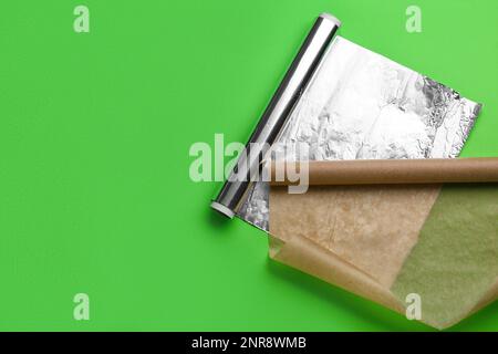 Rollen aus Aluminiumfolie und Backpapier auf grünem Hintergrund Stockfoto