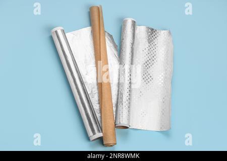 Rollen aus Aluminiumfolie und Backpapier auf farbigem Hintergrund Stockfoto