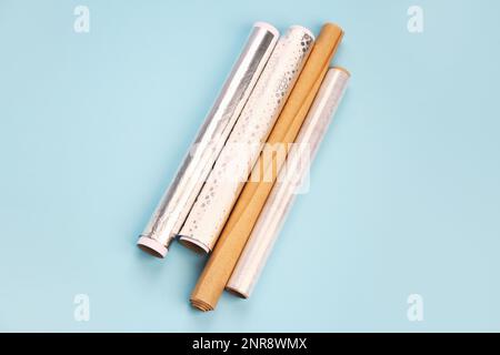 Rollen aus Aluminiumfolie, Backpapier und Lebensmittelfolie auf farbigem Hintergrund Stockfoto