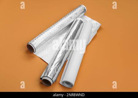 Rollen aus Aluminiumfolie und Backpapier auf orangefarbenem Hintergrund Stockfoto
