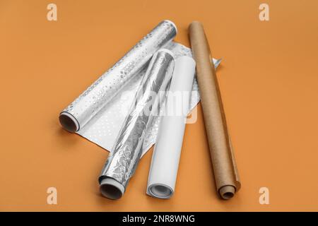 Rollen aus Aluminiumfolie und Backpapier auf orangefarbenem Hintergrund Stockfoto