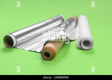 Rollen aus Aluminiumfolie und Backpapier auf grünem Hintergrund Stockfoto
