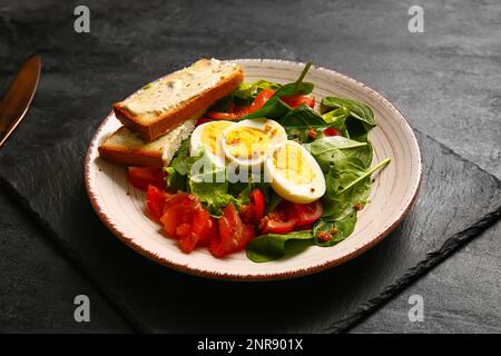 Teller mit köstlichem Salat mit gekochten Eiern, Lachs- und Frischkäse-Sandwiches auf schwarzem Grunge-Hintergrund Stockfoto