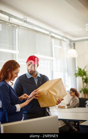 Pünktlich wie immer. Eine junge Frau, die ein Paket von einem Deliveryman in ihrem Büro erhält. Stockfoto