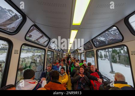 WENGEN, SCHWEIZ, 13,1.2023: Viele Menschen in einem Panoramawagen der Jungfrau-Zahnradbahn auf dem Weg auf den Gipfel des Berges. Stockfoto