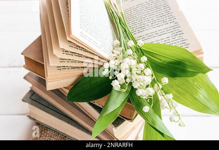 Ein Stapel alter Bücher und ein Strauß von Frühlingslilien des Tals auf einem offenen Buch. Vorderansicht. Frühlingszusammensetzung mit Blumen. Guten Morgen Stockfoto