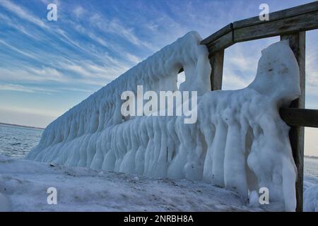 Blick auf eine gefrorene Anlegestelle in Travemünde in Deutschland mit dicken Eiszapfen auf dem Geländer und dem wolkigen Himmel in klarem Blau. Stockfoto