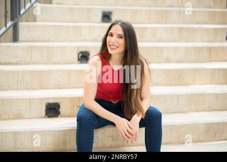 Schöne Frau, die auf der Treppe sitzt und vor der Tür lächelt Stockfoto