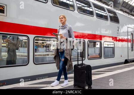 Junge Frau, die vor einem Intercity-Zug der Deutschen Bahn steht (Modell freigegeben) Stockfoto