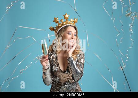 Glückliche Frau mit Champagner und herabfallenden Serpentinen auf hellblauem Hintergrund Stockfoto