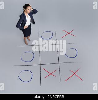 Junge Frau und Darstellung des Tic-tac-Toe-Spiels auf grauem Hintergrund, über der Sicht. Konzept der Geschäftsstrategie Stockfoto