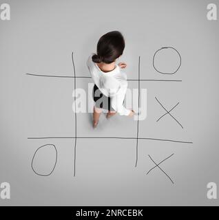 Junge Frau und Darstellung des Tic-tac-Toe-Spiels auf grauem Hintergrund, über der Sicht. Konzept der Geschäftsstrategie Stockfoto