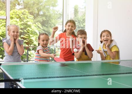 Süße glückliche Kinder, die drinnen Tischtennis spielen Stockfoto