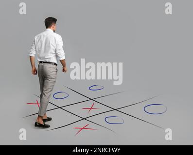 Mann und Darstellung des Tic-tac-Toe-Spiels auf grauem Hintergrund, Rückansicht. Konzept der Geschäftsstrategie Stockfoto