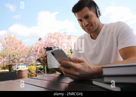 Glücklicher Mann mit Smartphone und Kaffee, der im Café im Freien ein Hörbuch hört Stockfoto