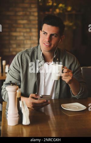 Mann mit Smartphone, der Hörbuch am Tisch im Café hört Stockfoto