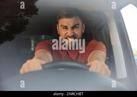 Emotionaler Mann im Auto, Blick durch die Windschutzscheibe. Aggressives Fahrverhalten Stockfoto