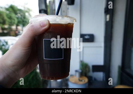 Nahaufnahme Hand mit Eisschwarz Americano in Plastikbecher zum Mitnehmen Stockfoto