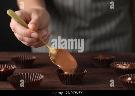 Professioneller Konditor, der köstliche Schokoladenbonbons am Holztisch herstellt, Nahaufnahme Stockfoto