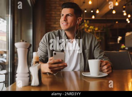 Mann mit Smartphone, der Hörbuch am Tisch im Café hört Stockfoto