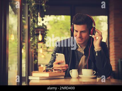 Mann mit Smartphone, der Hörbuch am Tisch im Café hört Stockfoto