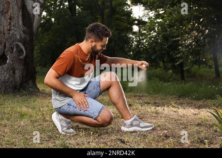 Ein Mann, der im Park Insektenschutzmittel auf das Bein aufträgt. Zeckenbissprophylaxe Stockfoto